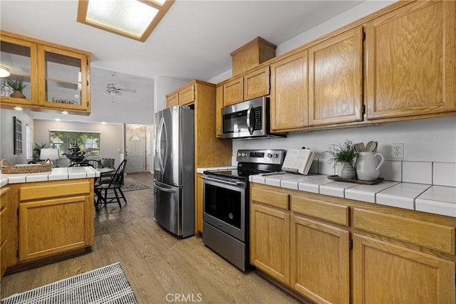 2081 Marilyn Dr, Chico, CA 95928 - kitchen featuring stainless steel appliances, light wood-style floors, vaulted ceiling, glass insert cabinets, and tile countertops