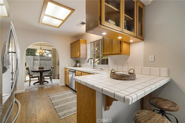 2081 Marilyn Dr, Chico, CA 95928 - kitchen with appliances with stainless steel finishes, light wood-style flooring, brown cabinets, arched walkways, and glass insert cabinets