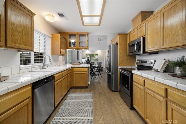 2081 Marilyn Dr, Chico, CA 95928 - kitchen with stainless steel appliances, wood finished floors, a peninsula, glass insert cabinets, and tile counters