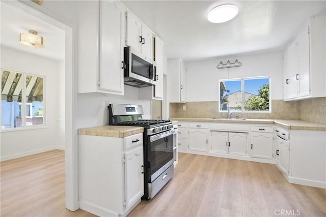 5609 Clark Ave, Lakewood, CA 90712 - kitchen with appliances with stainless steel finishes, light wood finished floors, backsplash, white cabinets, and tile countertops