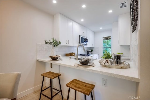 321 Orange Blossom Unit 166, Irvine, CA 92618 - kitchen with stainless steel microwave, decorative backsplash, a peninsula, white cabinets, and recessed lighting