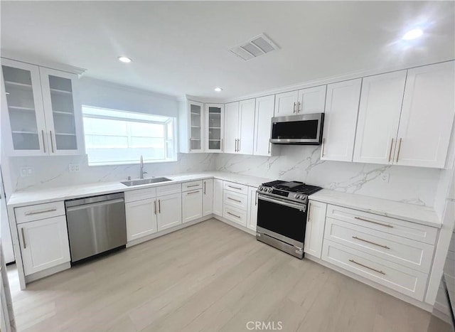 21541 Yucatan Ave, Woodland Hills, CA 91364 - kitchen with appliances with stainless steel finishes, light wood-type flooring, decorative backsplash, white cabinetry, and glass insert cabinets