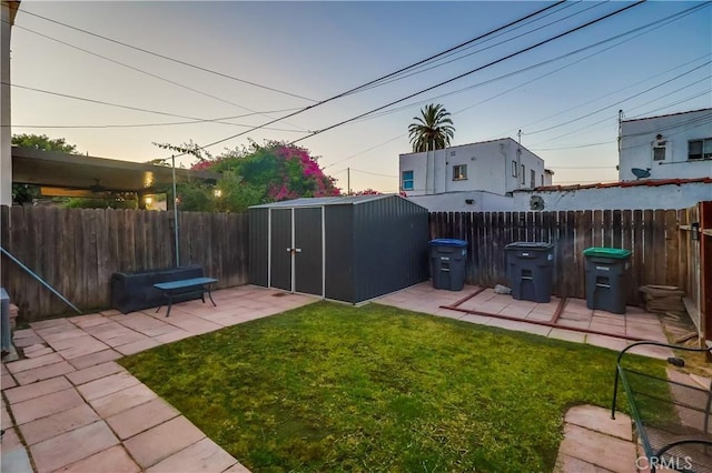2975 Fernwood Ave, Lynwood, CA 90262 - yard at dusk featuring a storage unit, a fenced backyard, and a patio area