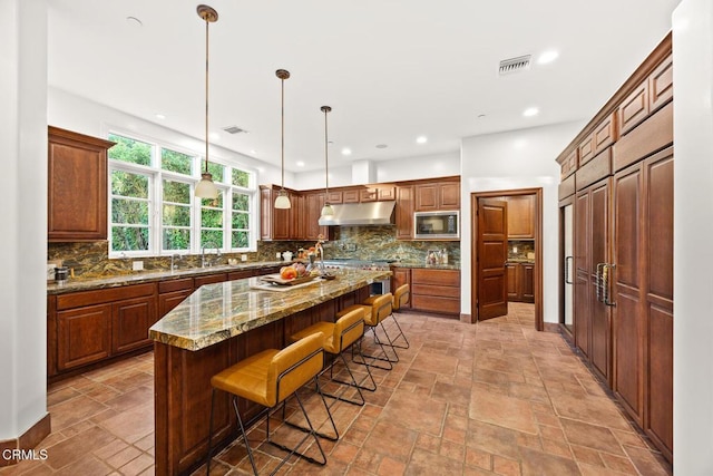 1533 Rancho Ave, Glendale, CA 91201 - kitchen with built in microwave, stone tile floors, tasteful backsplash, under cabinet range hood, and a breakfast bar