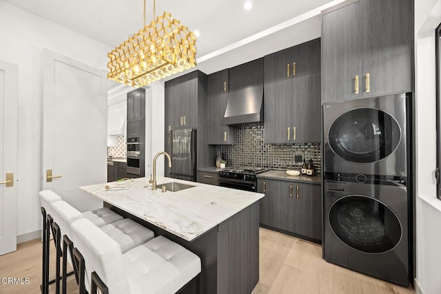 4828 Oakwood Ave, La Canada Flintridge, CA 91011 - kitchen featuring stacked washer / dryer, black gas range, light wood-style floors, decorative backsplash, and a center island with sink