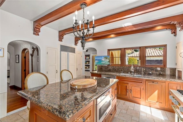 1811 N Flower St, Santa Ana, CA 92706 - kitchen with arched walkways, beamed ceiling, stone tile flooring, stove, and dark stone counters