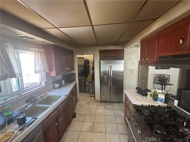 1409 E 41st Pl, Los Angeles, CA 90011 - kitchen featuring appliances with stainless steel finishes, tile counters, light tile patterned flooring, under cabinet range hood, and a paneled ceiling