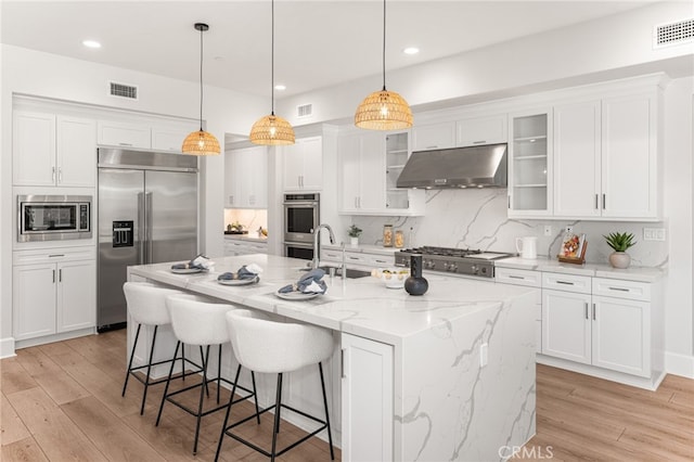 13428 Silver Sky Rd, Rancho Cucamonga, CA 91739 - kitchen featuring built in appliances, under cabinet range hood, light wood-type flooring, white cabinetry, and tasteful backsplash