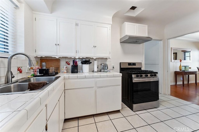 2118 W 84th St, Los Angeles, CA 90047 - kitchen with stainless steel gas range, tile countertops, white cabinets, tasteful backsplash, and exhaust hood
