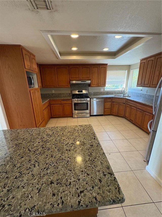 429 S Hill St, Orange, CA 92869 - kitchen featuring stainless steel appliances, a raised ceiling, brown cabinetry, under cabinet range hood, and recessed lighting