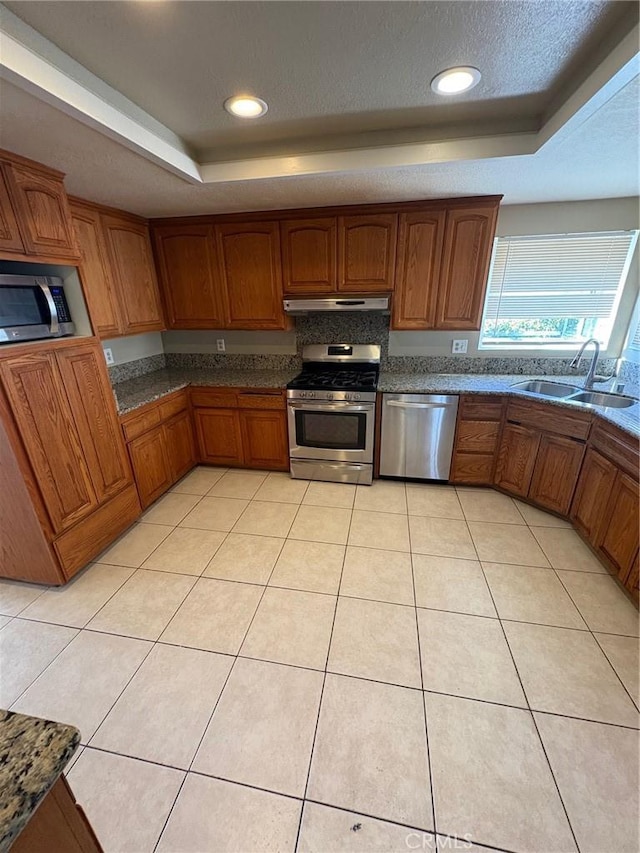 429 S Hill St, Orange, CA 92869 - kitchen featuring appliances with stainless steel finishes, a tray ceiling, brown cabinets, under cabinet range hood, and light tile patterned floors
