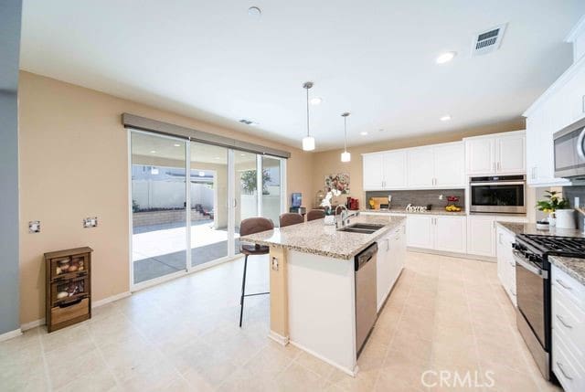 30106 Stargazer Way, Menifee, CA 92584 - kitchen with appliances with stainless steel finishes, a breakfast bar, white cabinetry, a center island with sink, and decorative light fixtures