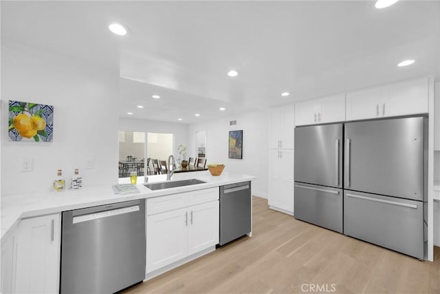 5042 Olympic Dr, Los Alamitos, CA 90720 - kitchen featuring appliances with stainless steel finishes, a peninsula, light wood-type flooring, white cabinets, and recessed lighting