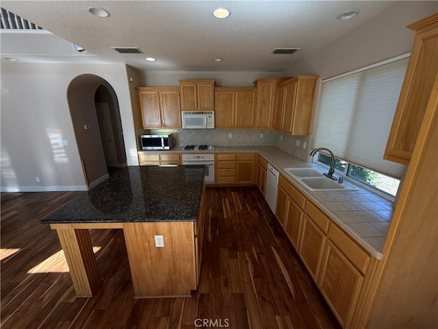 4125 Sattui Ct, Merced, CA 95348 - kitchen with white appliances, dark wood-style flooring, arched walkways, decorative backsplash, and a kitchen island