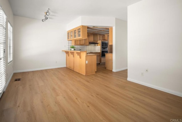 3531 Columbia St, San Diego, CA 92103 - kitchen featuring a peninsula, a breakfast bar, decorative backsplash, glass insert cabinets, and light wood-style floors