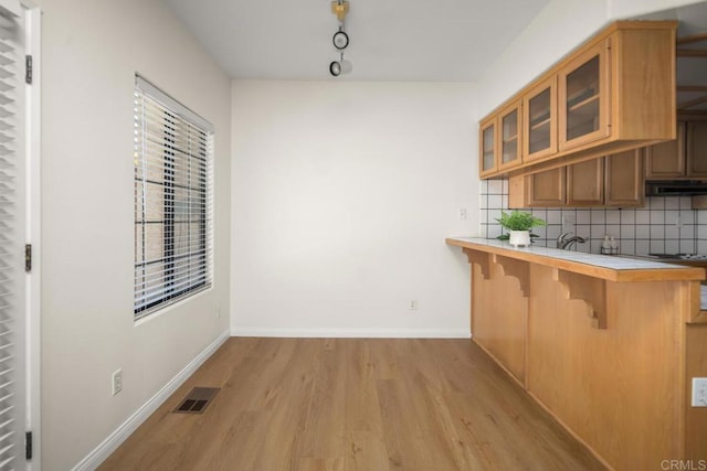 3531 Columbia St, San Diego, CA 92103 - kitchen with light wood-style floors, a kitchen bar, decorative backsplash, glass insert cabinets, and under cabinet range hood