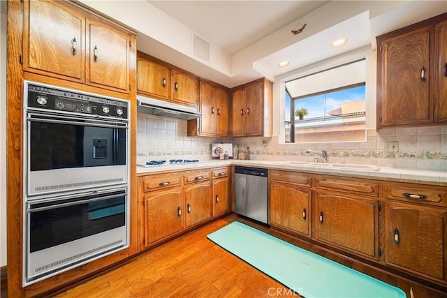 2008 S Bentley Ave Unit 5, Los Angeles, CA 90025 - kitchen with white appliances, under cabinet range hood, light wood-type flooring, brown cabinets, and decorative backsplash