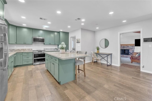6721 E Coralite St, Long Beach, CA 90808 - kitchen featuring green cabinetry, appliances with stainless steel finishes, a center island, a breakfast bar area, and light stone countertops