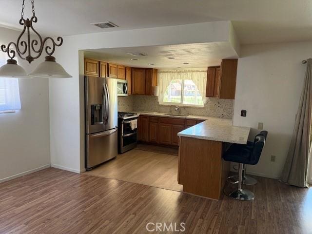 15163 Tournament Dr, Helendale, CA 92342 - kitchen featuring appliances with stainless steel finishes, brown cabinetry, a peninsula, and light wood-style flooring