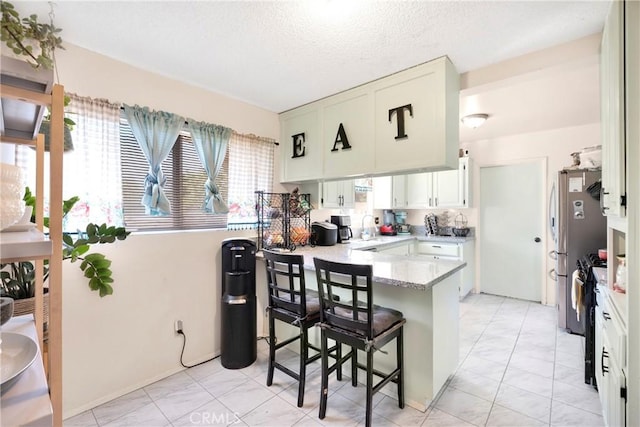 10000 8th Ave, Hesperia, CA 92345 - kitchen featuring a peninsula, light marble finish floors, a breakfast bar, white cabinets, and a textured ceiling