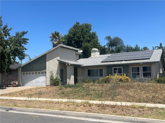 946 W Woodcrest, Bloomington, CA 92316 - view of front facade featuring roof mounted solar panels, concrete driveway, a garage, stucco siding, and a chimney