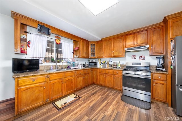 795 E 42nd Pl, Los Angeles, CA 90011 - kitchen featuring stainless steel appliances, under cabinet range hood, brown cabinets, wood finished floors, and light stone counters