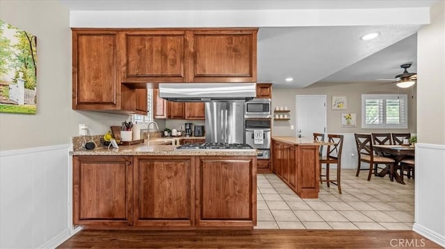 1052 Golden Rain St, Upland, CA 91786 - kitchen featuring a peninsula, stainless steel appliances, brown cabinetry, a ceiling fan, and wainscoting