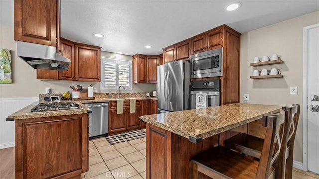 1052 Golden Rain St, Upland, CA 91786 - kitchen with stainless steel appliances, a peninsula, under cabinet range hood, light stone counters, and a breakfast bar area
