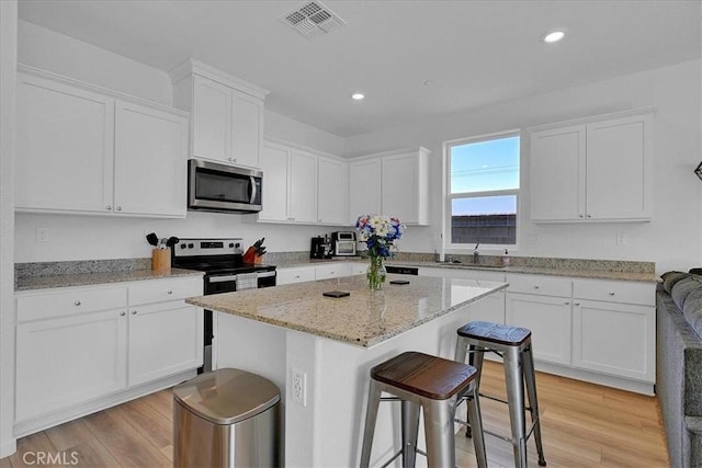 5516 Sunhaven St, Marysville, CA 95901 - kitchen with appliances with stainless steel finishes, white cabinetry, a breakfast bar area, light wood-type flooring, and recessed lighting