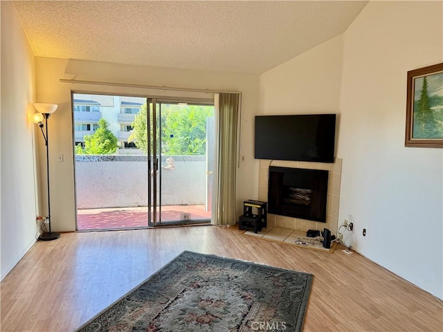 7640 Oso Ave Unit 316, Winnetka, CA 91306 - living area featuring wood finished floors, a tiled fireplace, vaulted ceiling, and a textured ceiling