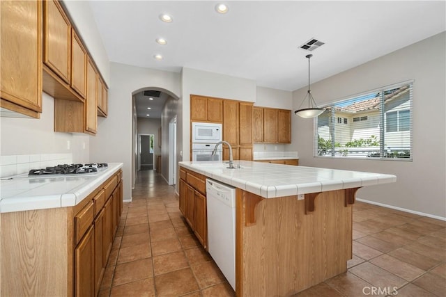 42730 Settlers Rdg, Murrieta, CA 92562 - kitchen with white appliances, arched walkways, recessed lighting, a kitchen island with sink, and brown cabinets