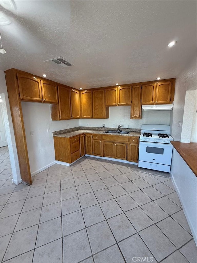 1032 W Coronado Ave, Ridgecrest, CA 93555 - kitchen featuring gas range gas stove, under cabinet range hood, brown cabinetry, a textured ceiling, and light tile patterned floors