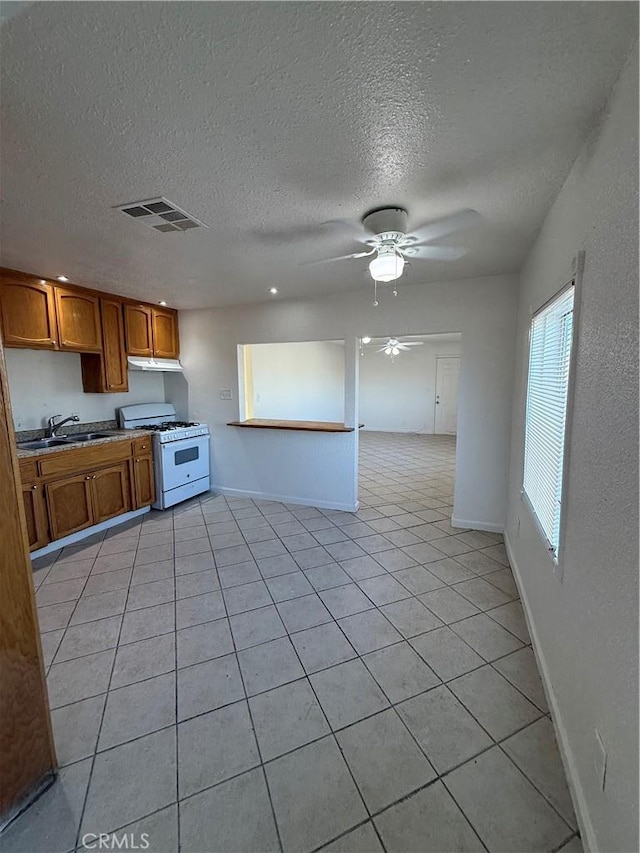 1032 W Coronado Ave, Ridgecrest, CA 93555 - kitchen featuring gas range gas stove, brown cabinetry, a ceiling fan, light tile patterned floors, and a textured ceiling