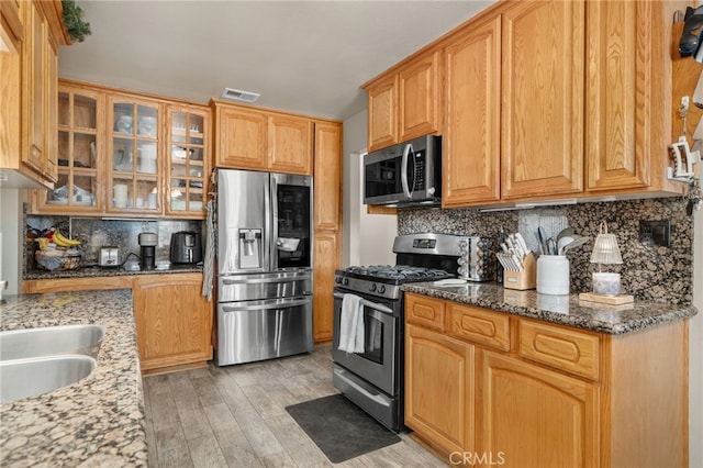 7420 London Ave, Rancho Cucamonga, CA 91730 - kitchen with appliances with stainless steel finishes, light wood-style floors, decorative backsplash, dark stone counters, and glass insert cabinets