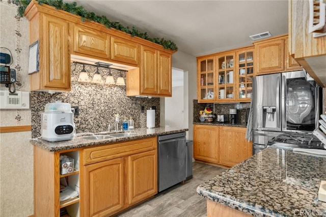 7420 London Ave, Rancho Cucamonga, CA 91730 - kitchen featuring appliances with stainless steel finishes, light wood-style floors, tasteful backsplash, glass insert cabinets, and dark stone counters