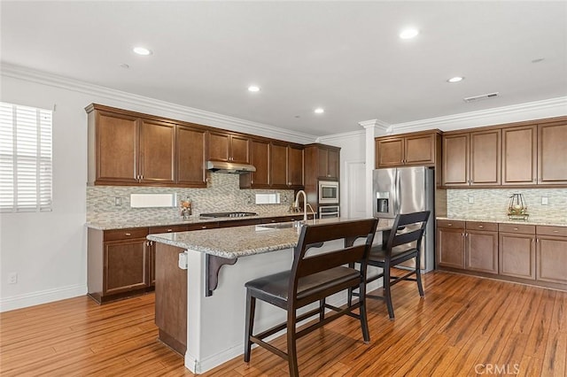 11905 Flicker Cv, Corona, CA 92883 - kitchen with under cabinet range hood, stainless steel appliances, light wood-type flooring, a kitchen breakfast bar, and tasteful backsplash
