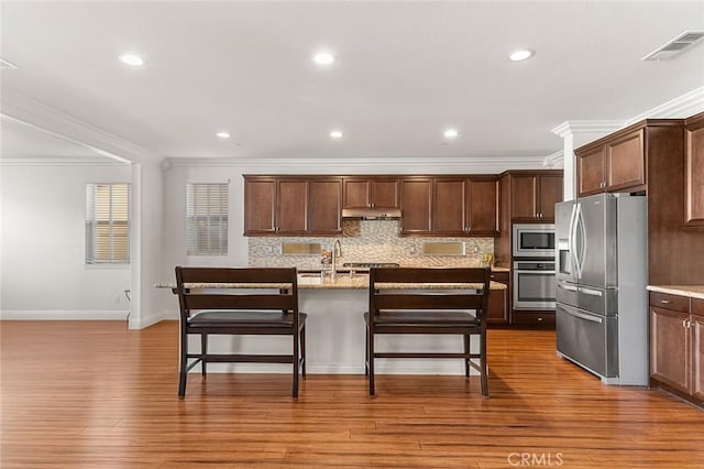 11905 Flicker Cv, Corona, CA 92883 - kitchen with stainless steel appliances, crown molding, a breakfast bar, backsplash, and a center island with sink