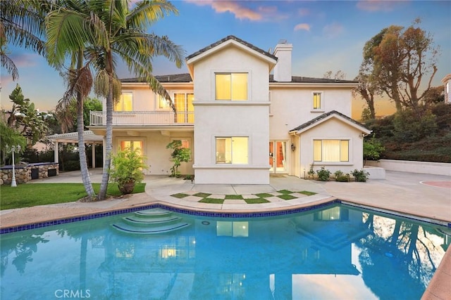 2832 Oak Knoll Dr, Diamond Bar, CA 91765 - back of property at dusk with a balcony, a chimney, a patio area, stucco siding, and an outdoor pool