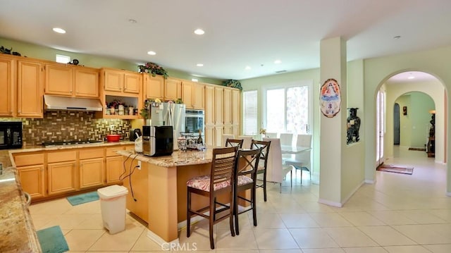 2056 Mission Hills Dr, Oxnard, CA 93036 - kitchen with under cabinet range hood, decorative backsplash, arched walkways, a kitchen island, and oven