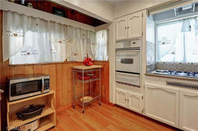 12108 Muriel Dr, Lynwood, CA 90262 - kitchen featuring white appliances, a warming drawer, light wood-type flooring, white cabinetry, and wooden walls