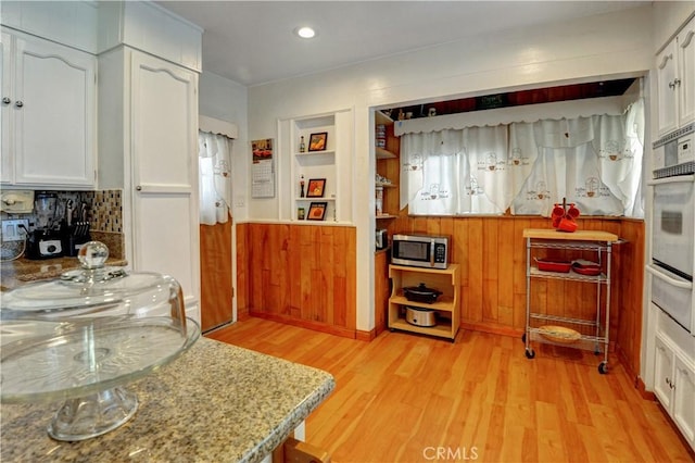 12108 Muriel Dr, Lynwood, CA 90262 - kitchen featuring a warming drawer, stainless steel microwave, light wood-style floors, white cabinetry, and oven