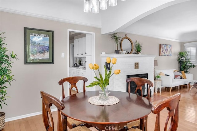 1269 W 1st St, San Pedro, CA 90732 - dining area with light wood-type flooring, a brick fireplace, crown molding, and a chandelier