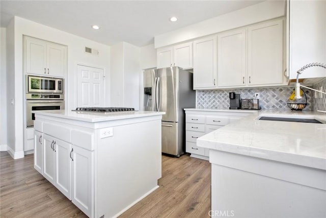 32197 Callesito Fadrique, Temecula, CA 92592 - kitchen featuring appliances with stainless steel finishes, light wood finished floors, backsplash, white cabinetry, and a center island