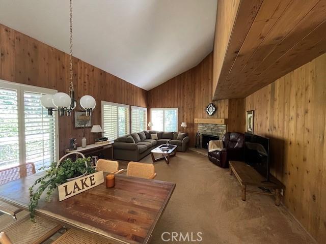 27821 Peninsula Dr, Lake Arrowhead, CA 92352 - dining room with wooden walls, lofted ceiling, a chandelier, a stone fireplace, and carpet floors