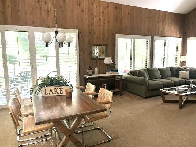 27821 Peninsula Dr, Lake Arrowhead, CA 92352 - carpeted dining room with wood walls, plenty of natural light, vaulted ceiling, and a chandelier