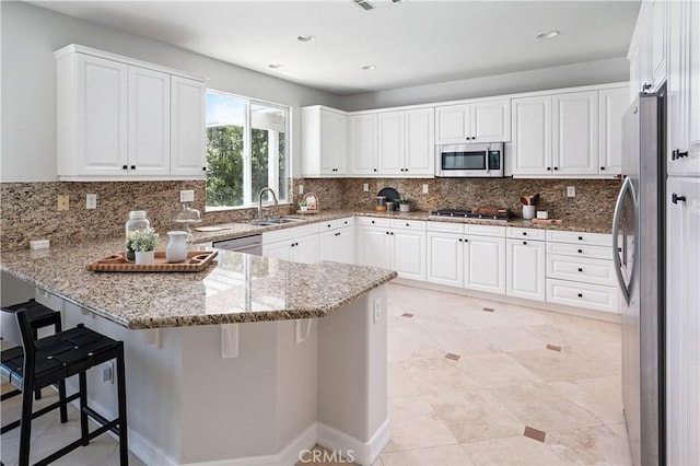 29125 Starwood Pl, Saugus, CA 91390 - kitchen featuring appliances with stainless steel finishes, a peninsula, backsplash, light stone counters, and white cabinetry