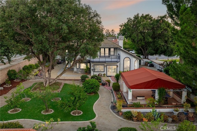 981 Deep Springs Dr, Claremont, CA 91711 - back of property at dusk with a balcony, stucco siding, a chimney, and a lawn