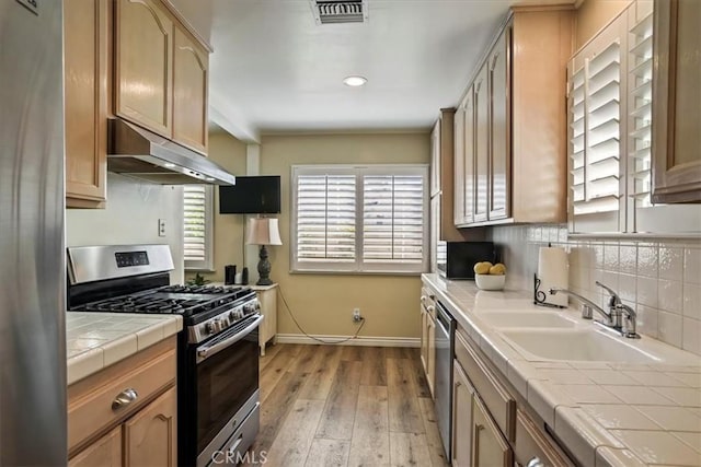 13239 Sayre St, Sylmar, CA 91342 - kitchen featuring stainless steel appliances, under cabinet range hood, tile countertops, light wood-style floors, and tasteful backsplash