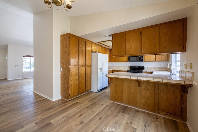43920 Delgado Ct, Lancaster, CA 93535 - kitchen featuring white fridge with ice dispenser, black microwave, brown cabinetry, stove, and tile countertops