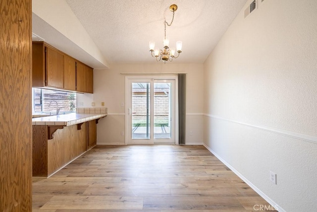 43920 Delgado Ct, Lancaster, CA 93535 - unfurnished dining area featuring a chandelier, light wood-type flooring, a textured ceiling, and vaulted ceiling